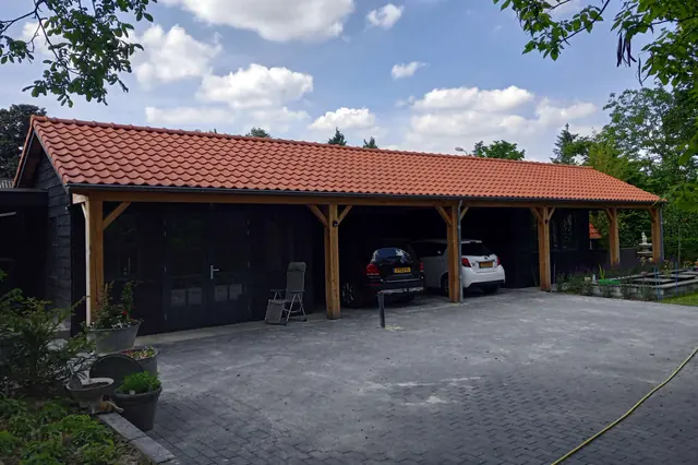 Overkapping met houten spanten en rood pannendak voor een zwart houten schuur in Berlicum